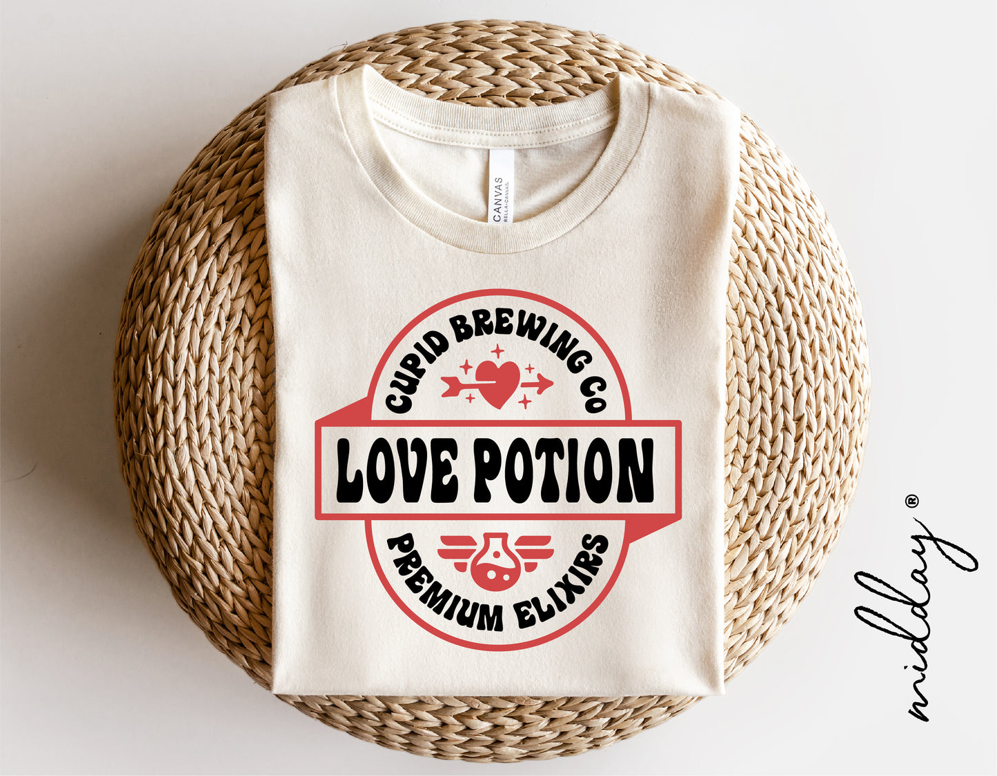 Cupid Brewing Co Love Potion t-shirt folded on wicker basket, featuring premium elixirs design with heart and wings.