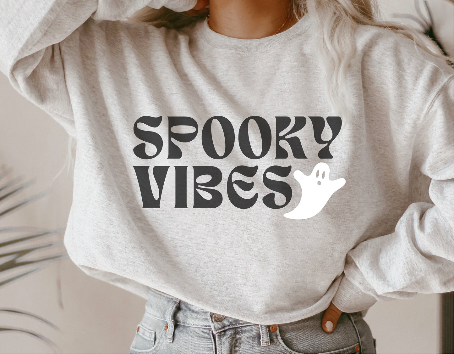 A woman wearing a grey sweatshirt featuring a "Spooky Vibes" design with a cute ghost graphic, perfect for Halloween and autumn decor.