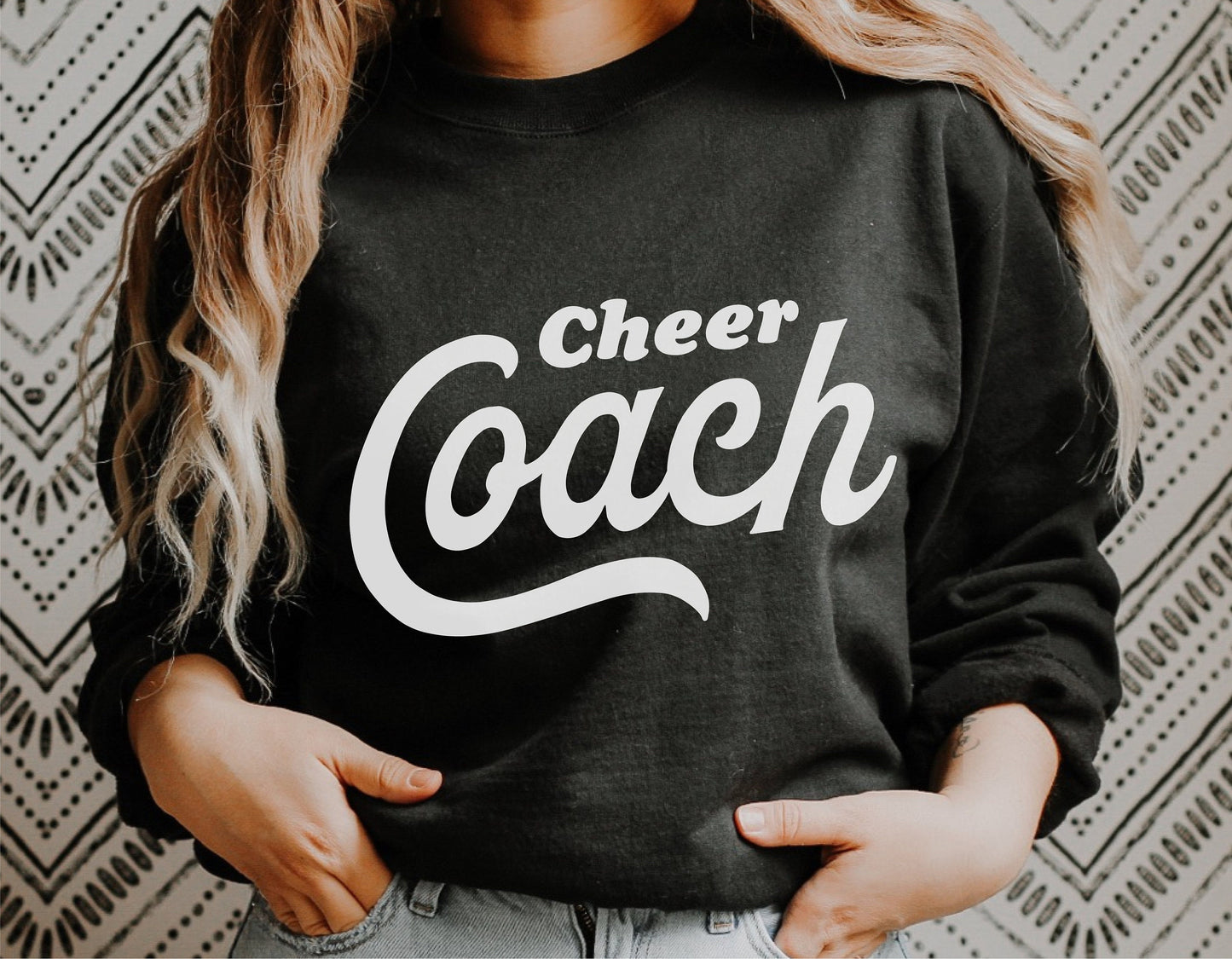 Black sweatshirt with white 'Cheer Coach' text, worn by individual, ideal for cheerleading coaches and team spirit apparel.