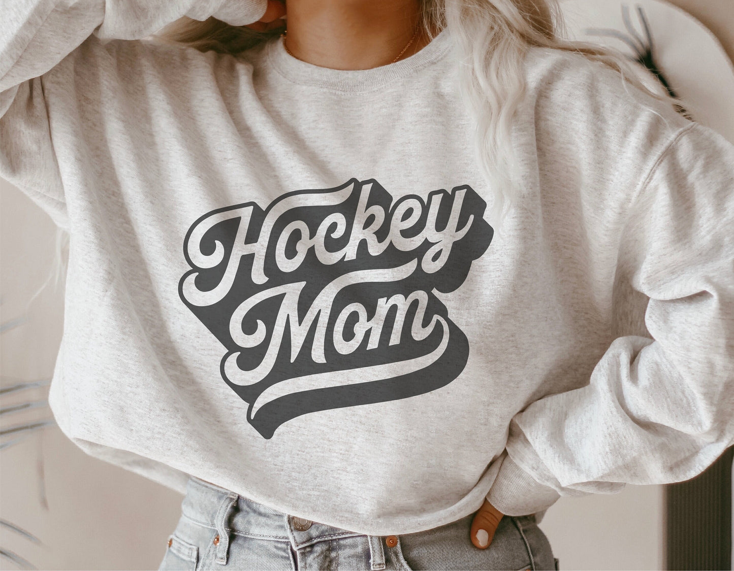Woman wearing a grey sweatshirt featuring a 'Hockey Mom' design, perfect for Cricut cut files and sublimation projects.