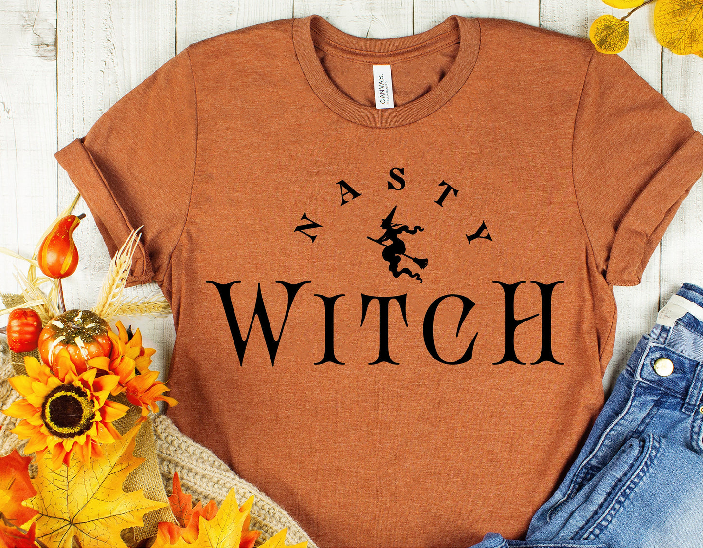 "Nasty Witch Halloween shirt with witch print, surrounded by autumn leaves and decor, ideal for spooky season fashion."