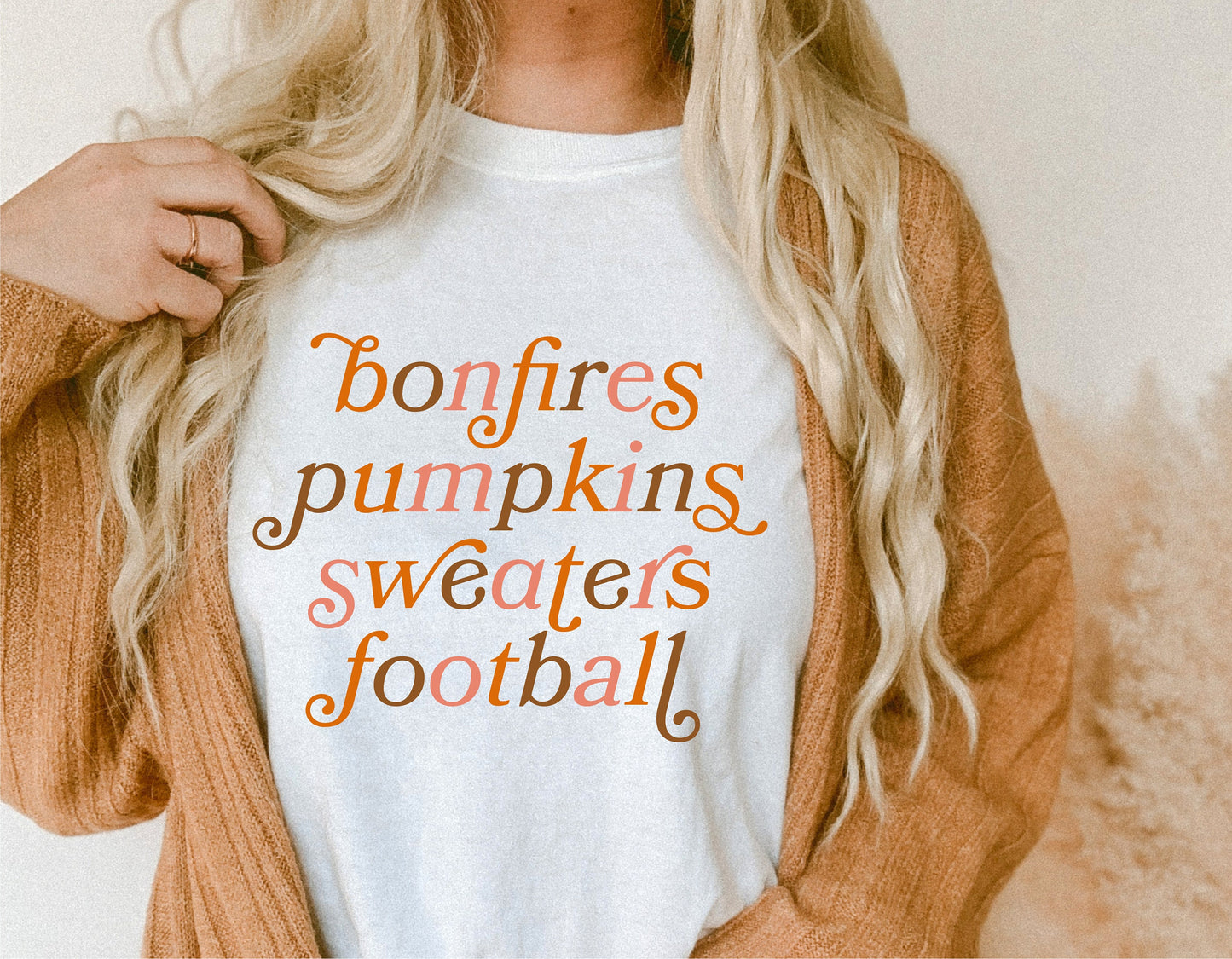 Woman wearing a fall-themed shirt with text: 'bonfires pumpkins sweaters football' for autumn and Halloween season.