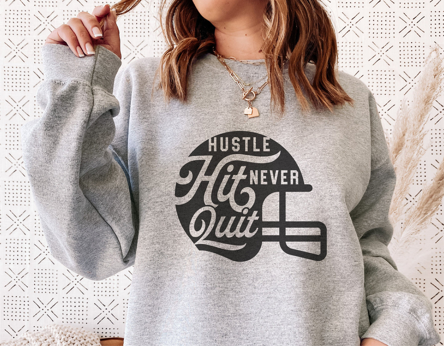Grey sweatshirt featuring 'Hustle Hit Never Quit' football helmet design, ideal for football enthusiasts and sports moms.