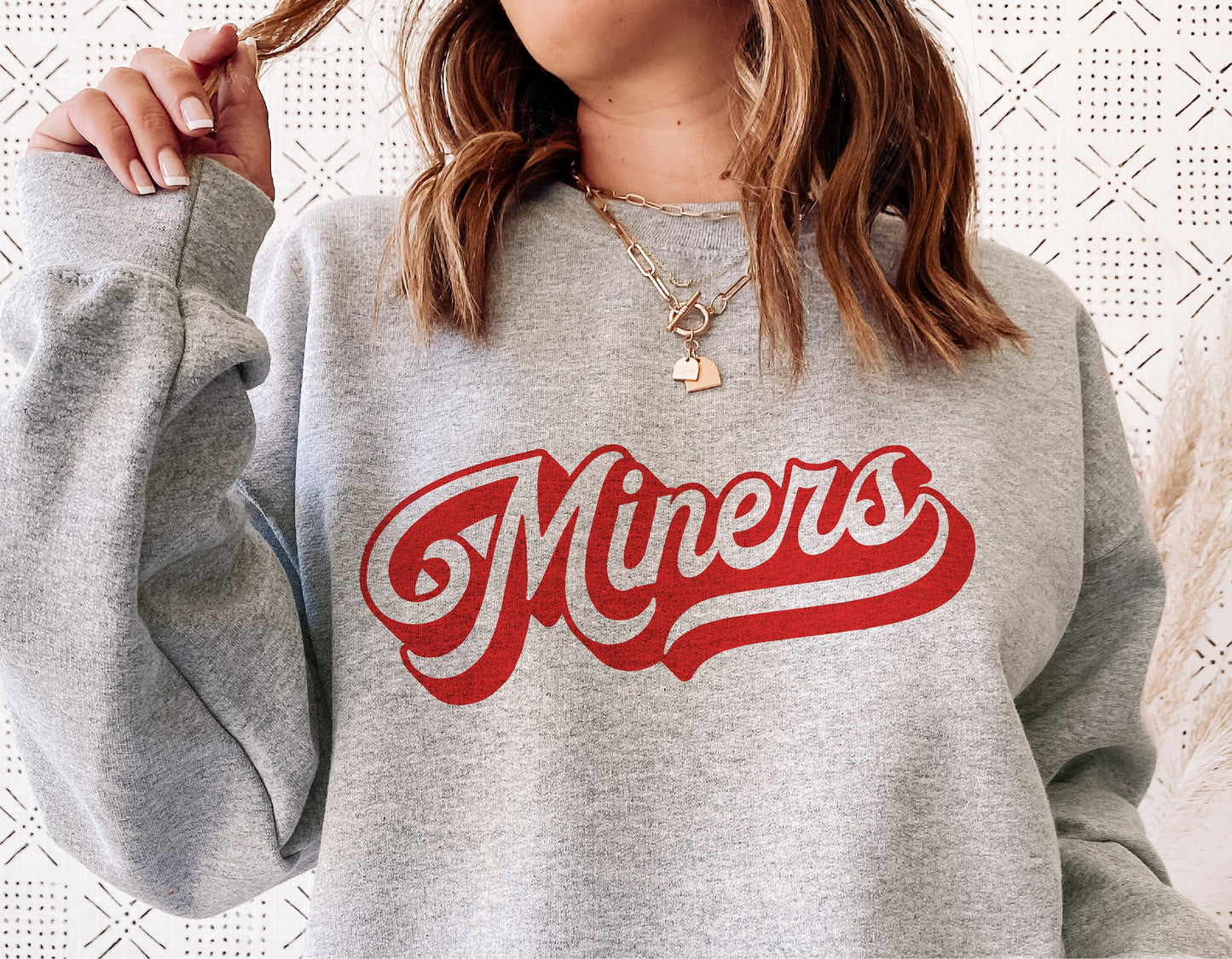 Woman wearing gray sweatshirt with red 'Miners' logo, showcasing school spirit and retro design for sports like football and basketball.
