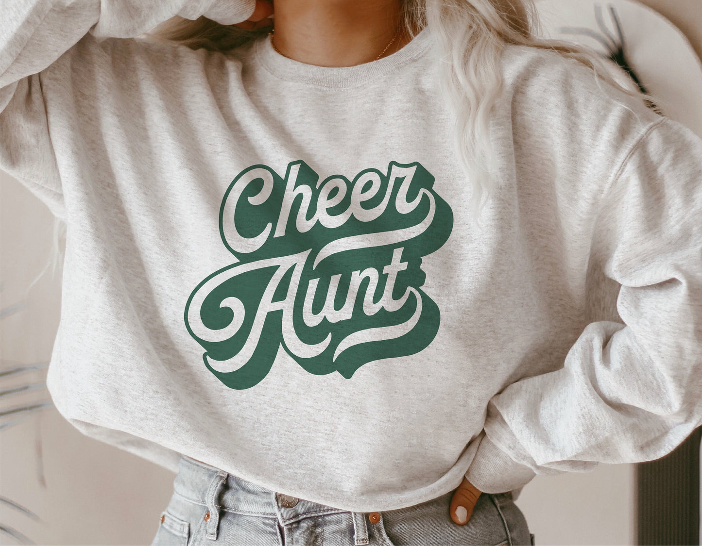 Woman wearing gray sweatshirt with 'Cheer Aunt' design, demonstrating team spirit and stylish silhouette for Cricut and crafting projects.