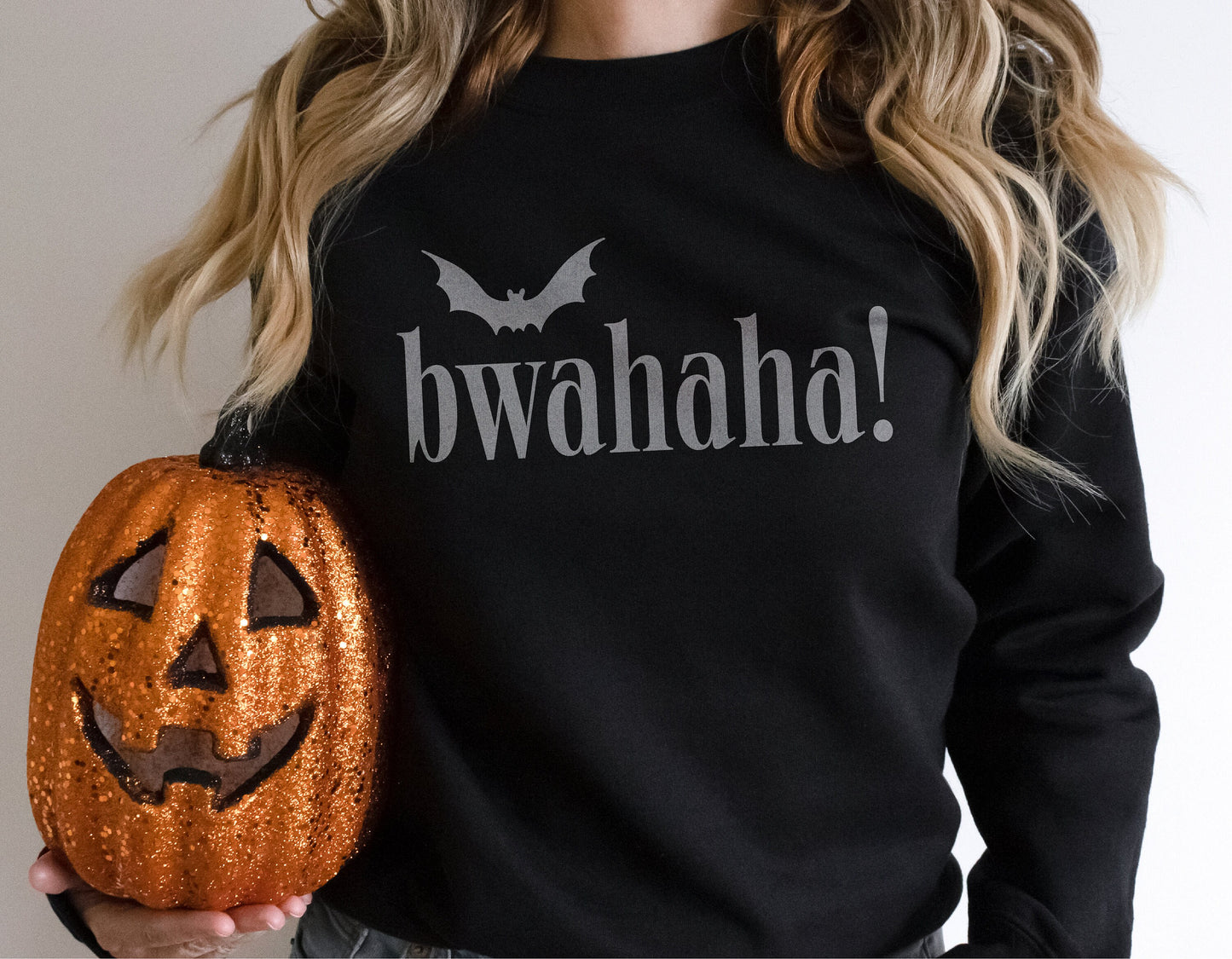 Person wearing black 'Bwahaha' Halloween shirt holding a glittery pumpkin.