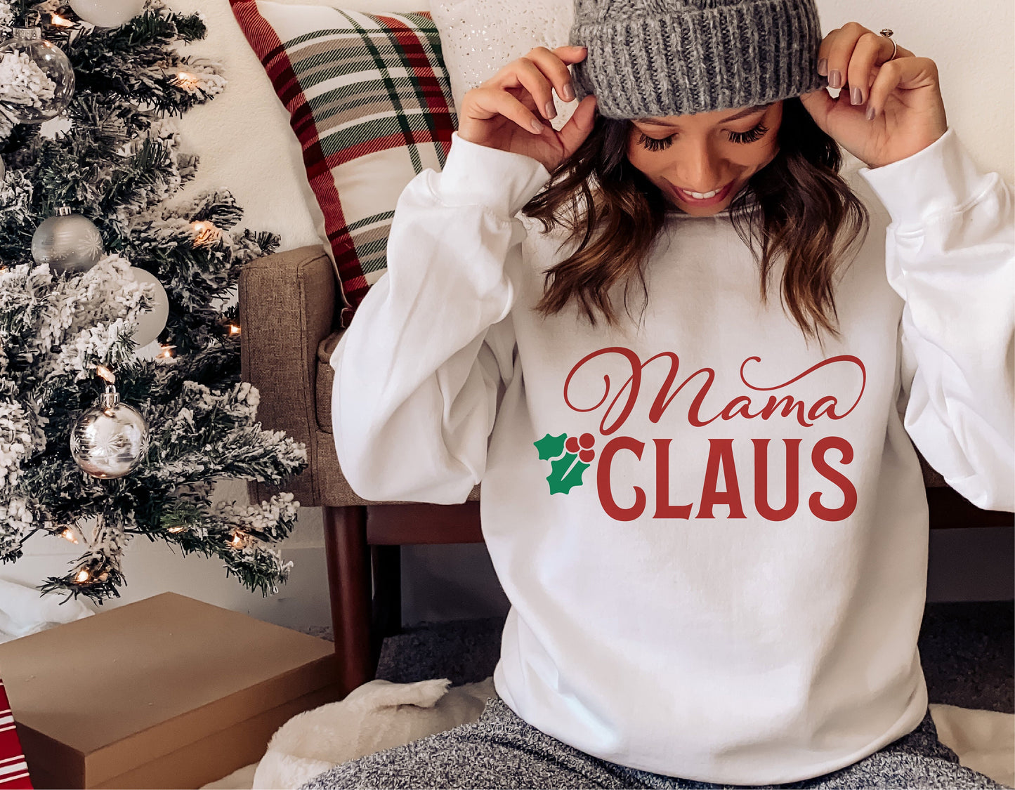 Woman wearing 'Mama Claus' Christmas holiday shirt by a decorated tree.
