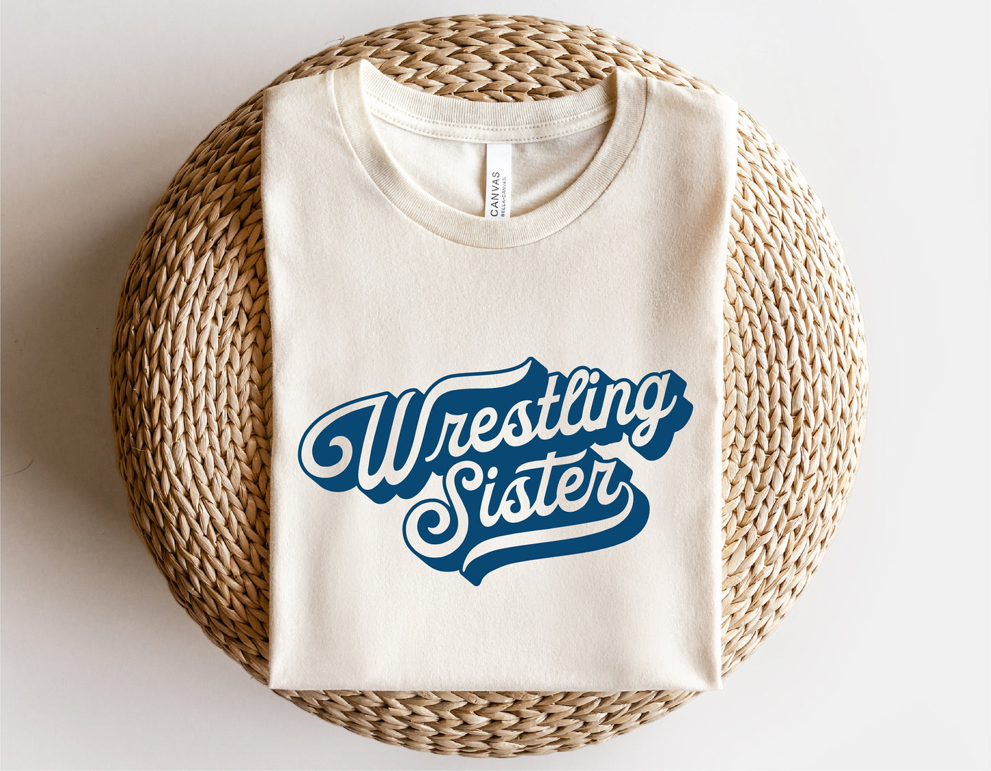 White T-shirt with 'Wrestling Sister' text design, laid on a woven basket background.