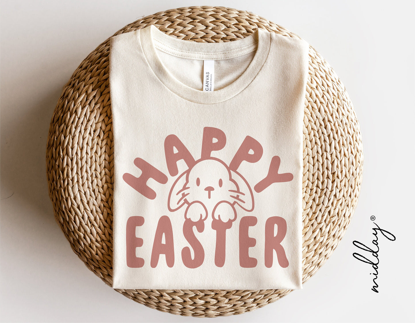 White t-shirt with 'Happy Easter' and cute bunny face design, perfect for Easter celebration, displayed on a woven mat.