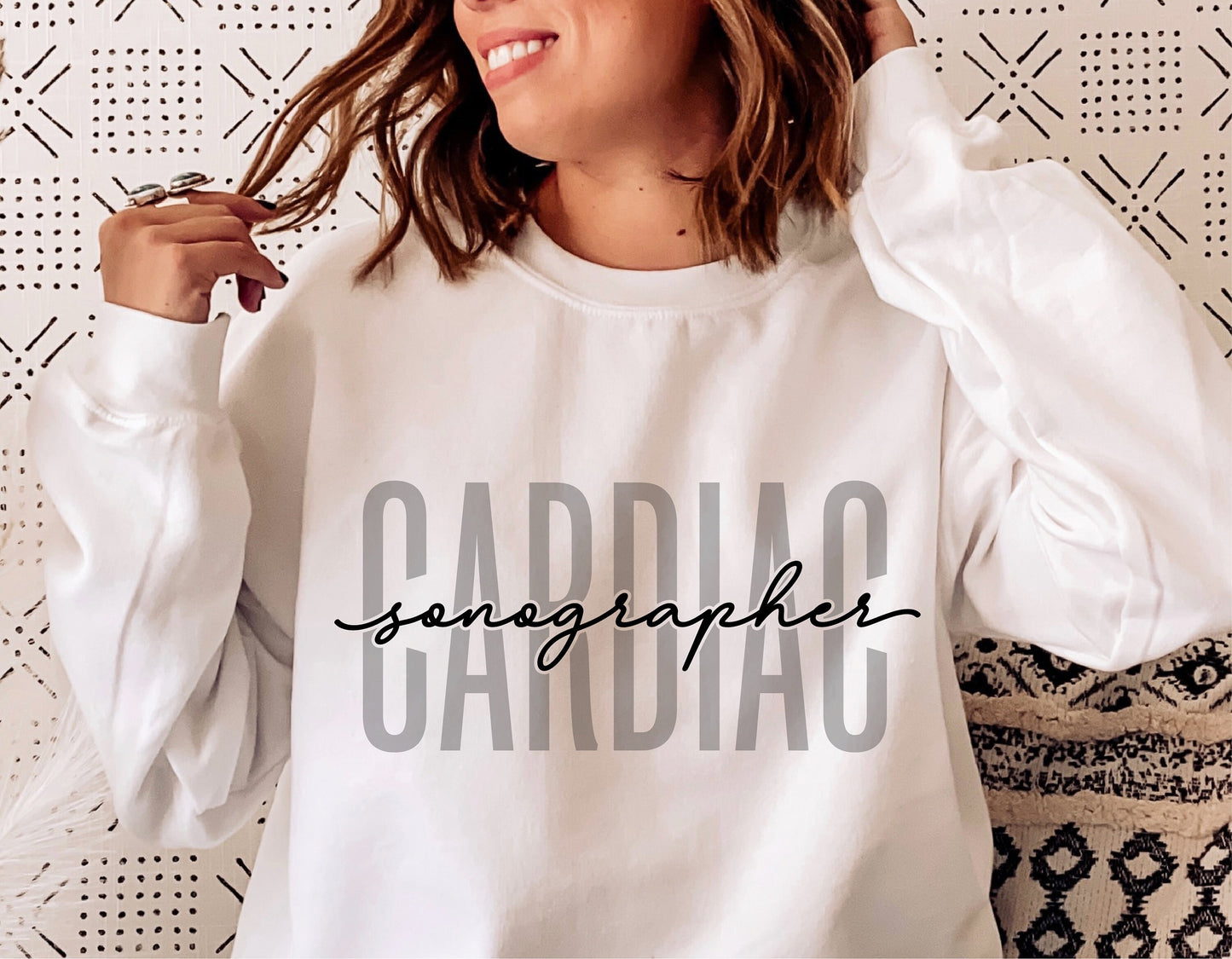 Woman wearing a white sweatshirt with 'Cardiac Sonographer' printed on the front, showcasing stylish design for healthcare professionals.