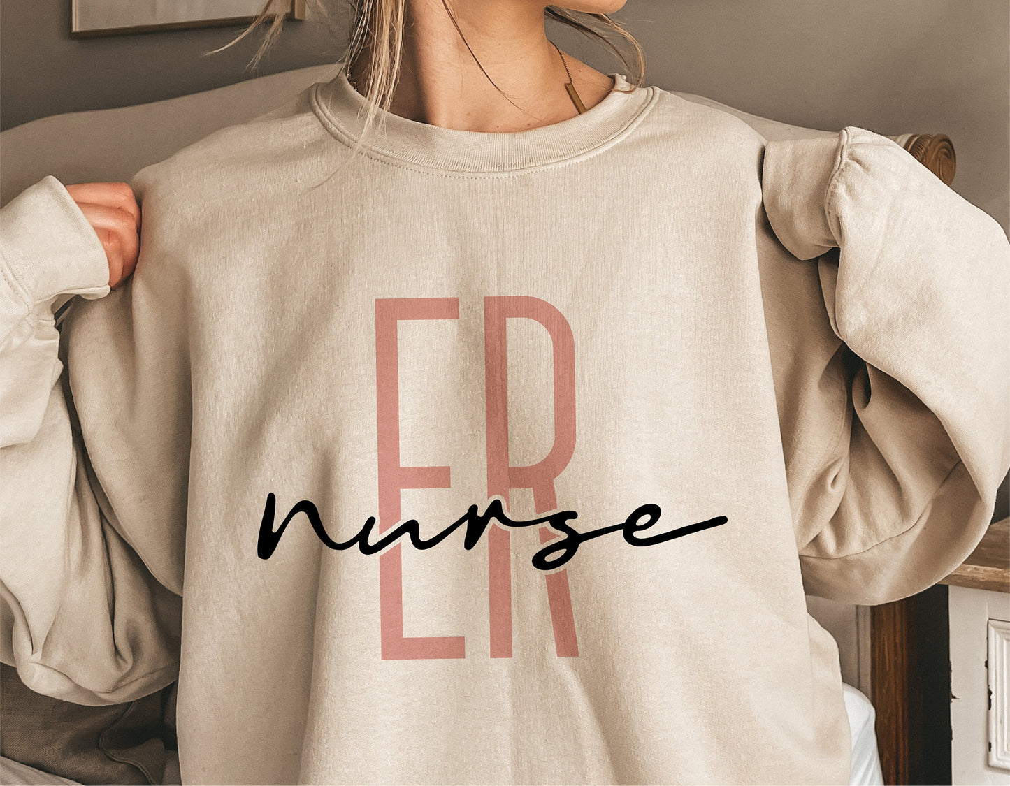 Person wearing a beige sweatshirt with 'ER Nurse' printed on the front in bold letters, showcasing nurse-themed apparel design.