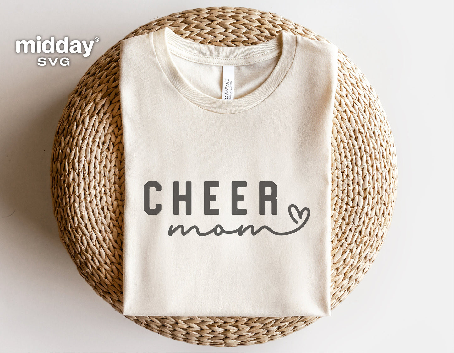 White t-shirt with 'Cheer Mom' text in black, folded on a woven mat for Cricut and silhouette projects.