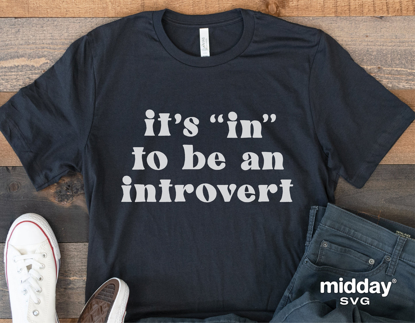 Black t-shirt with 'It's "in" to be an introvert' text, laid flat with sneakers and jeans for funny sarcastic fashion emphasis.