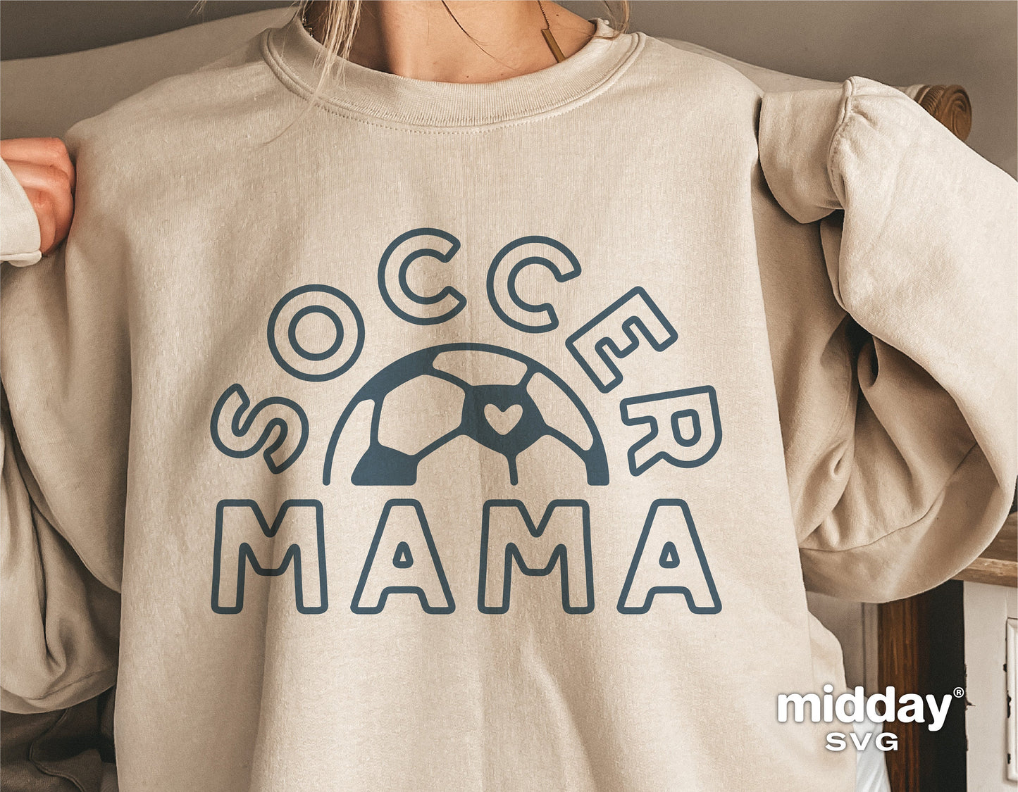 Woman wearing beige "Soccer Mama" sweatshirt with heart soccer ball design, perfect for sports moms and Cricut projects.