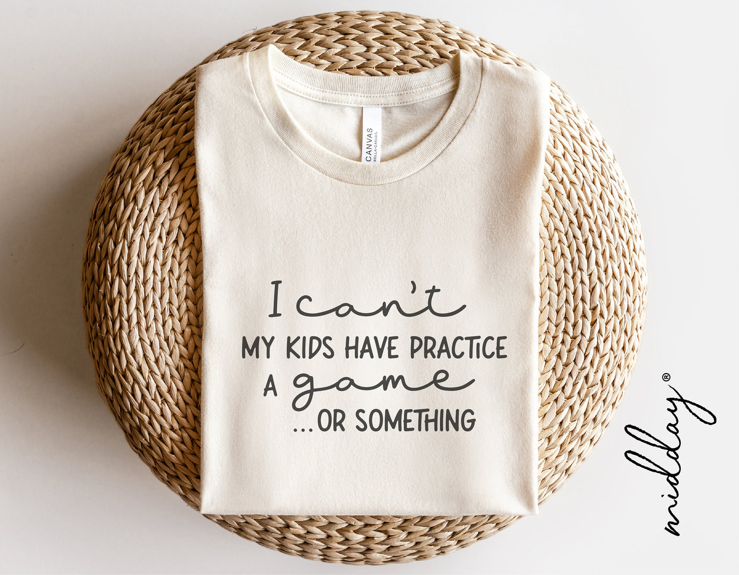 White t-shirt with text 'I can't, my kids have practice, a game or something' on a woven mat.