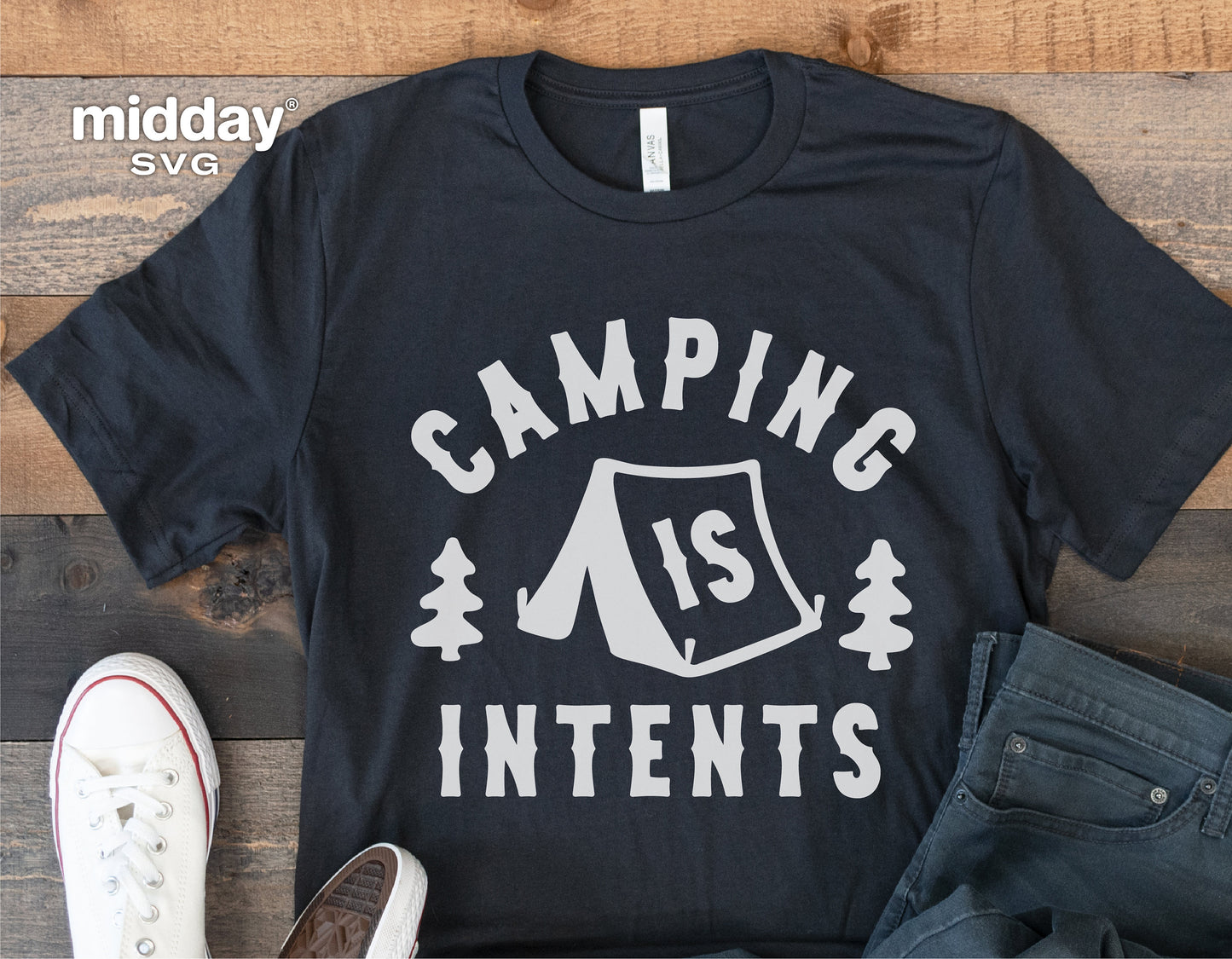 Black t-shirt with 'Camping is Intents' design, featuring a tent and trees, laid out on wooden surface with casual shoes and jeans.