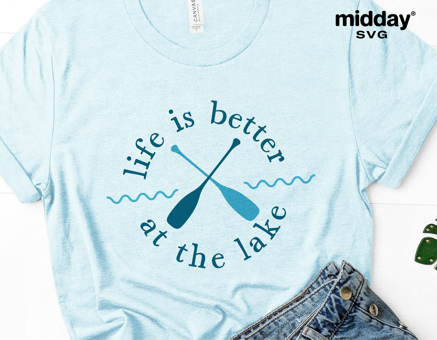 Light blue t-shirt with 'Life is better at the lake' design featuring crossed paddles, ideal for lake vacation or camping enthusiasts.