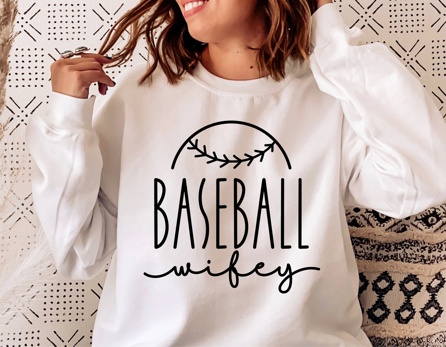 Woman wearing a white sweatshirt with a 'Baseball Wifey' design, ideal for baseball lovers.