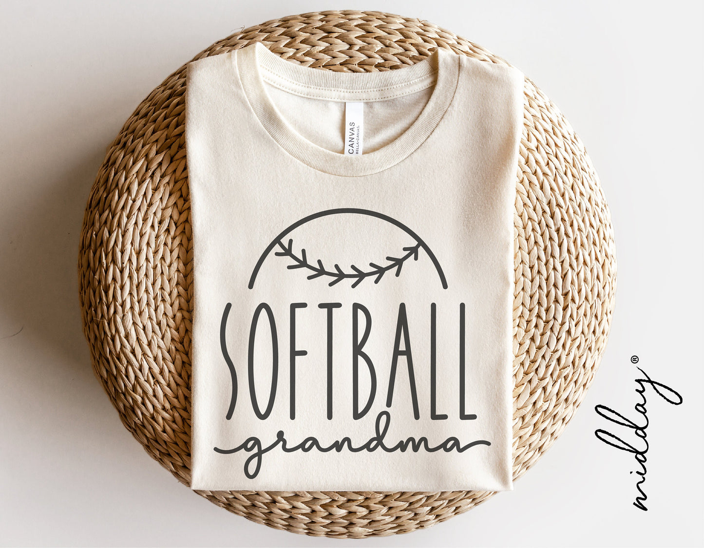 White cotton shirt with 'Softball Grandma' text and softball design, perfect for Cricut or Silhouette crafts, displayed on woven mat.