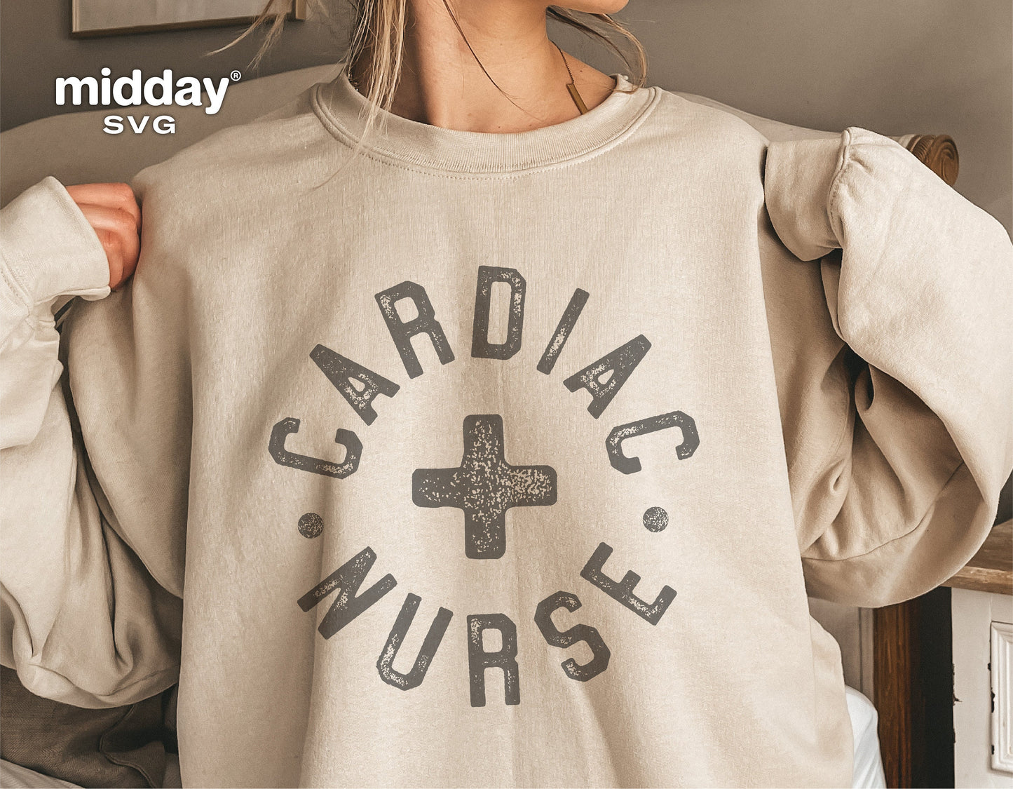Woman wearing beige sweater with 'Cardiac Nurse' graphic design, featuring a medical cross symbol.