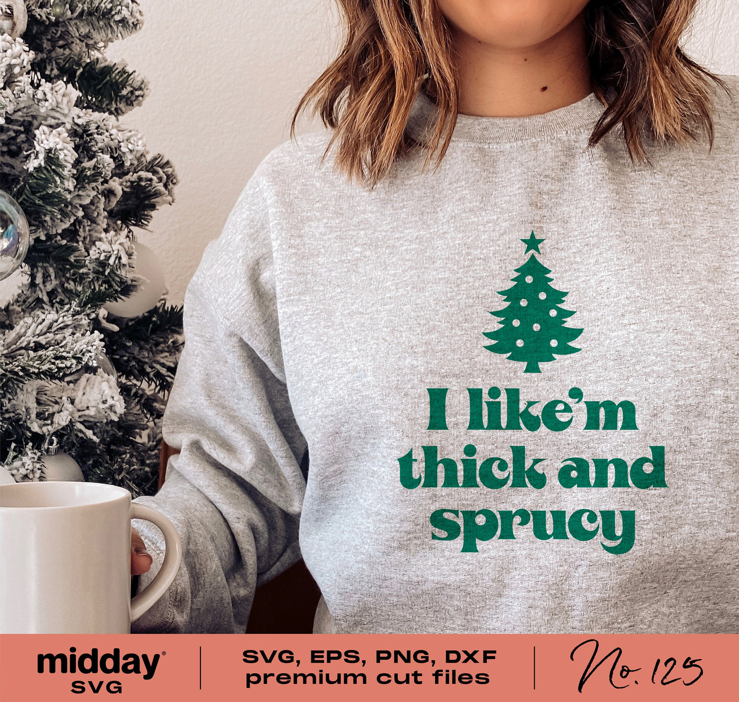 Woman wearing a gray shirt with 'I like 'em thick and sprucy' and Christmas tree graphic, holding a mug by a decorated tree.