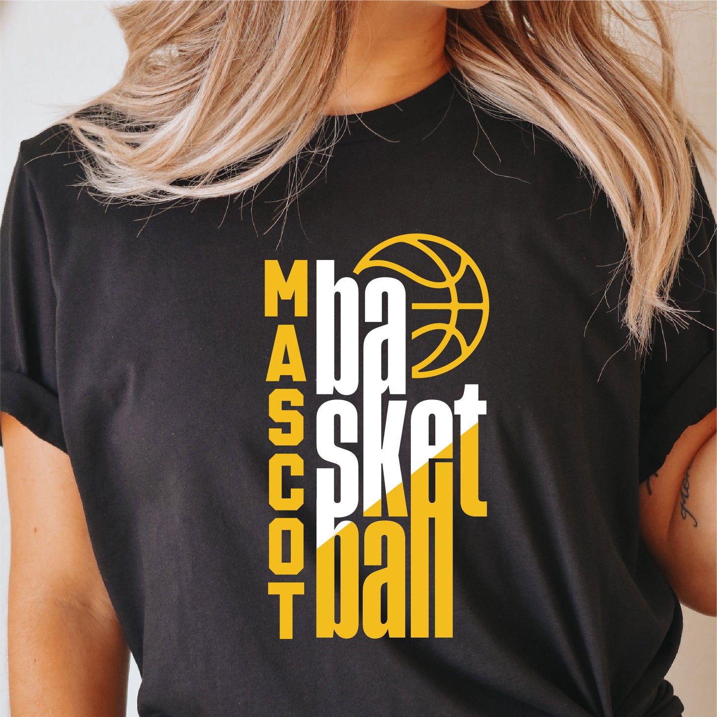 Person wearing black T-shirt with yellow and white basketball team graphic design, featuring words 'Mascot Basketball'. Ideal for Cricut and Silhouette.