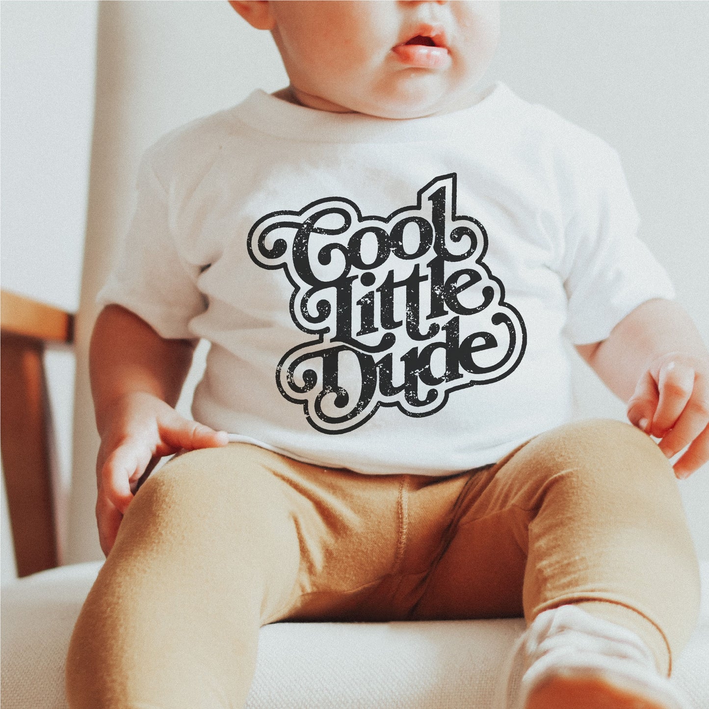 Baby wearing a white onesie with 'Cool Little Dude' design, sitting on a chair. Perfect for Cricut and Silhouette projects.