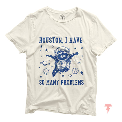 White t-shirt with 'Houston, I Have So Many Problems' and a distressed raccoon astronaut, floating in space, surrounded by stars and planets.