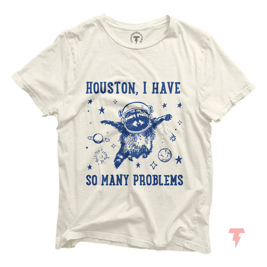 White t-shirt with 'Houston, I Have So Many Problems' and a distressed raccoon astronaut, floating in space, surrounded by stars and planets.