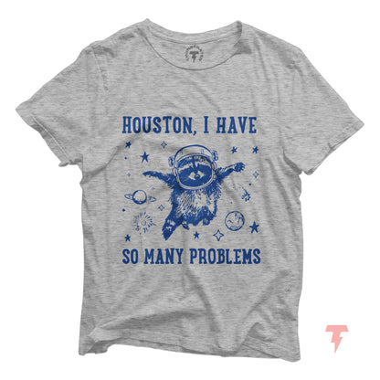 Grey t-shirt with a stressed raccoon astronaut and text 'Houston, I Have So Many Problems' in blue, depicting humor in chaos.