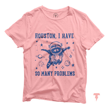 Pink t-shirt with 'Houston, I Have So Many Problems' featuring a raccoon astronaut in space, embracing chaotic fun.