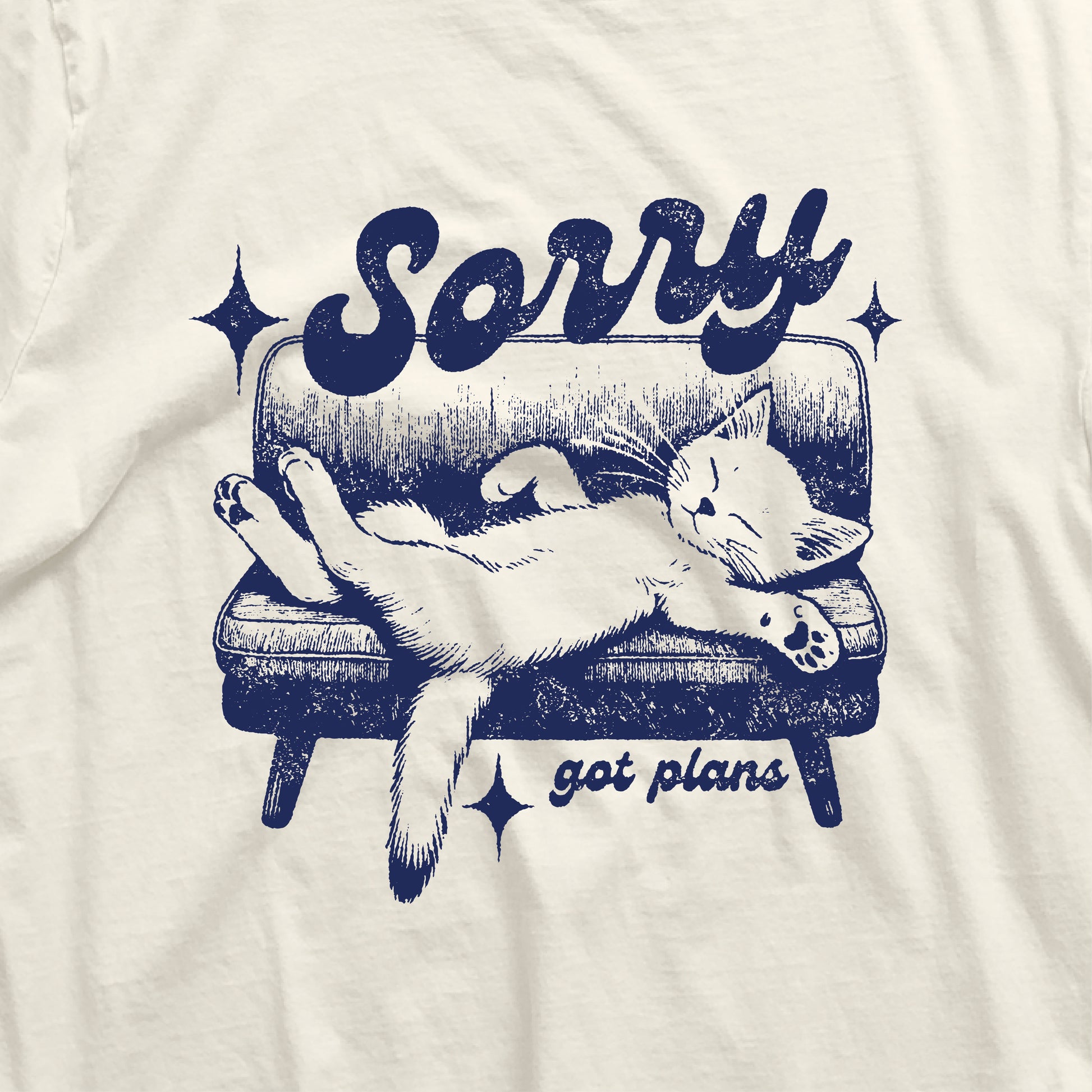 Cat relaxes on couch with 'Sorry, got plans' text on a funny t-shirt for cat lovers, perfect gift for introverts and animal enthusiasts.
