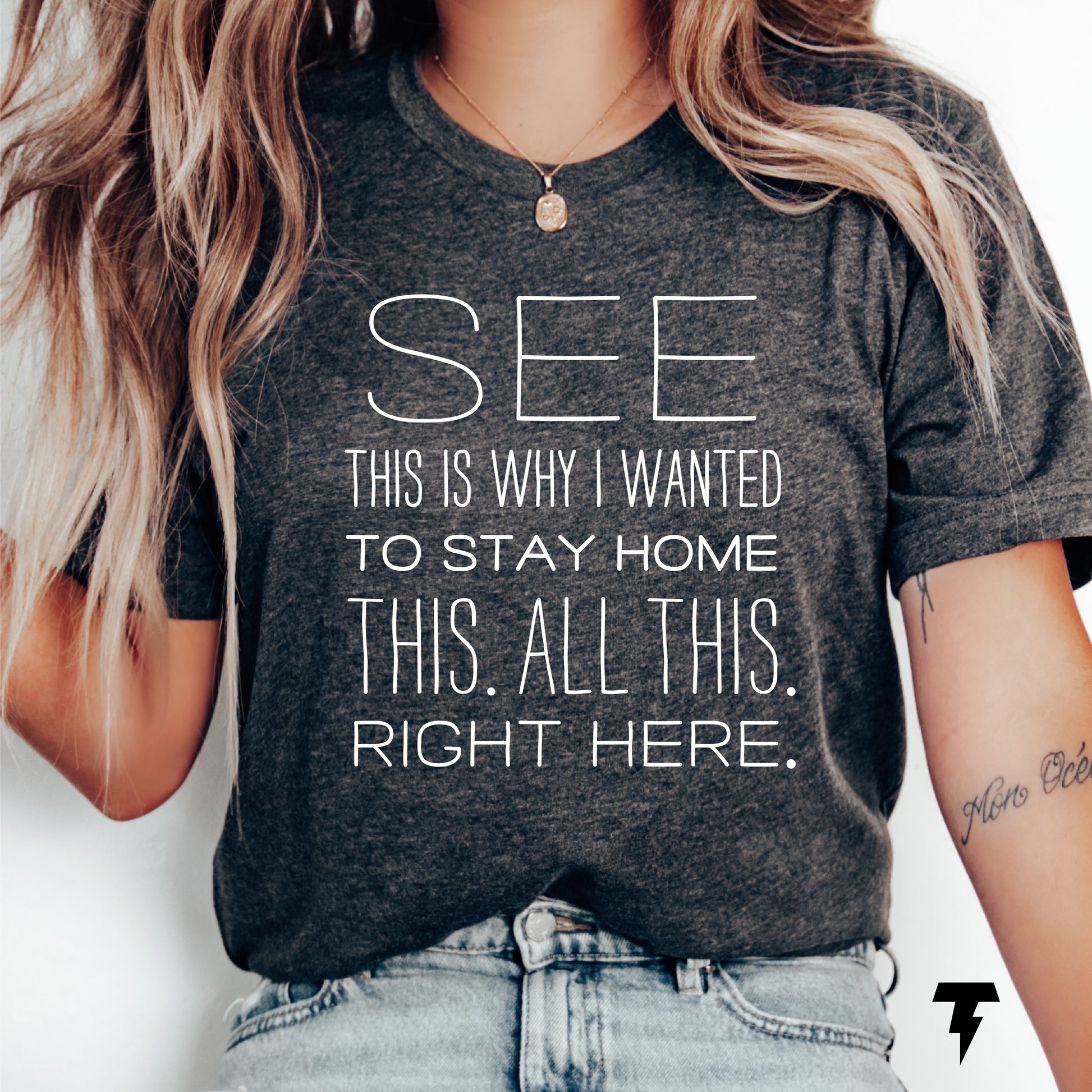 Woman wearing gray funny graphic tee with 'See This Is Why I Wanted To Stay Home' text, casual style, jeans.