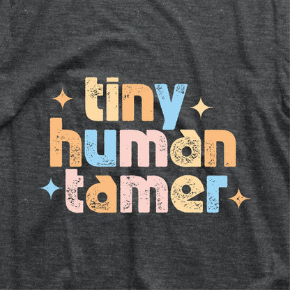 "Tiny Human Tamer" shirt in colorful font on dark fabric, ideal for pre-k and kindergarten teachers. Lightweight, breathable cotton.