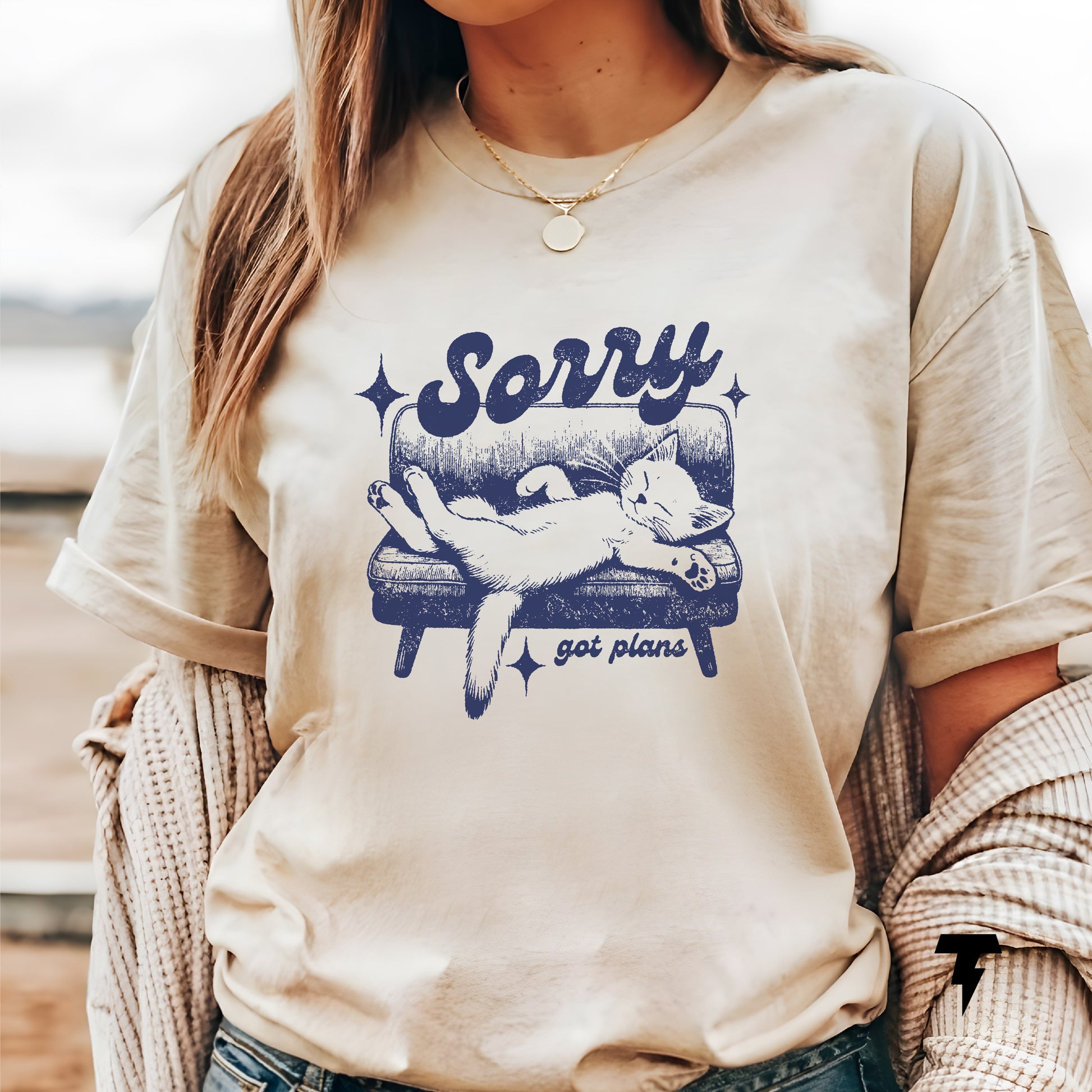 Woman wearing a beige "Sorry, got plans" funny cat t-shirt, perfect gift for cat lovers, featuring a relaxed cat graphic on a couch.