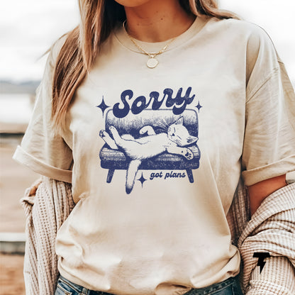 Woman wearing a beige "Sorry, got plans" funny cat t-shirt, perfect gift for cat lovers, featuring a relaxed cat graphic on a couch.
