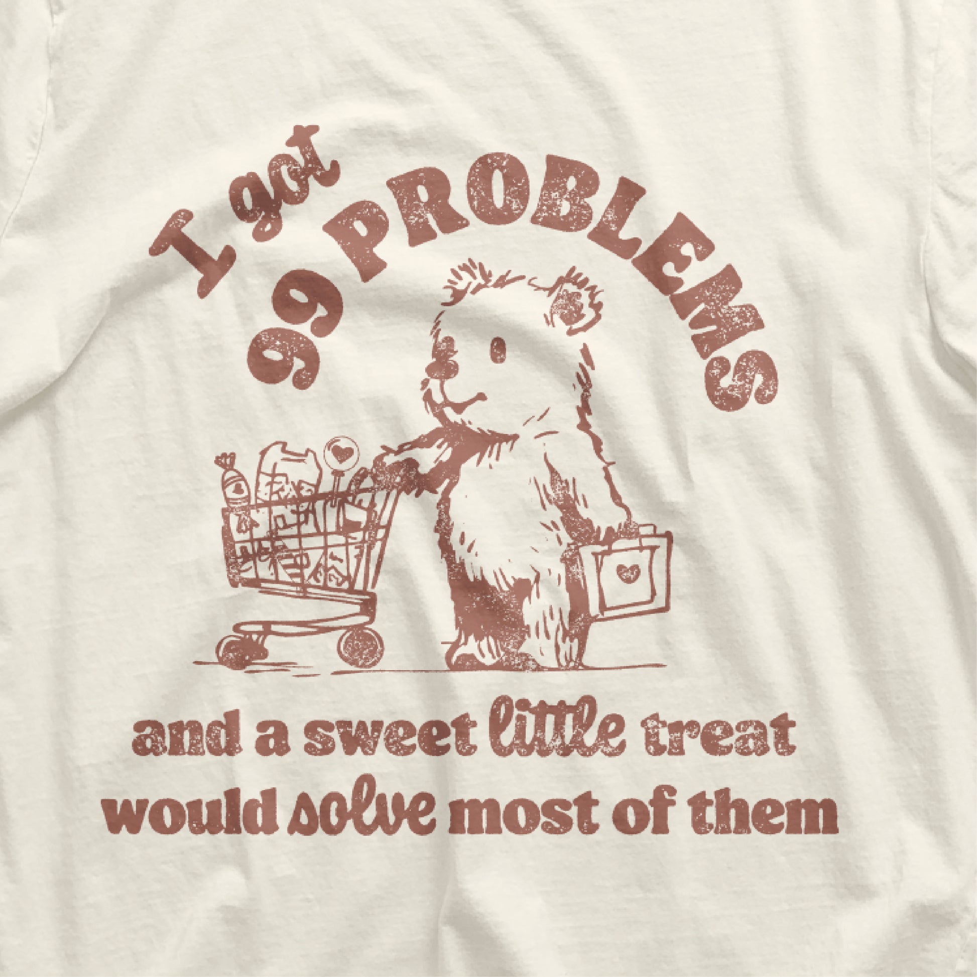 Vintage t-shirt with a cartoon bear, shopping cart, and humorous text '99 Problems and a Sweet Little Treat Would Solve Most of Them'