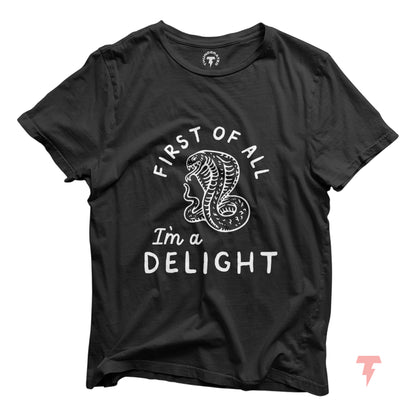 Black unisex t-shirt with 'First of all I'm a delight' text and a cobra graphic, made of soft Airlume cotton by Bella+Canvas.