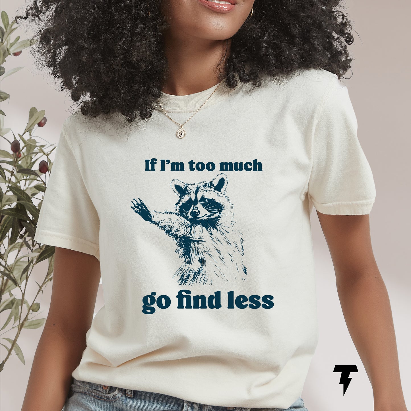 Woman wearing a T-shirt with a sarcastic raccoon saying 'If I'm too much go find less', perfect funny gift for raccoon lovers.