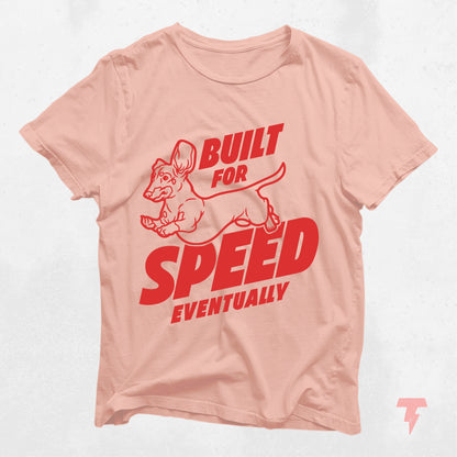 "Built for Speed Eventually" dachshund shirt in light pink with red text, cute gift for dog moms.