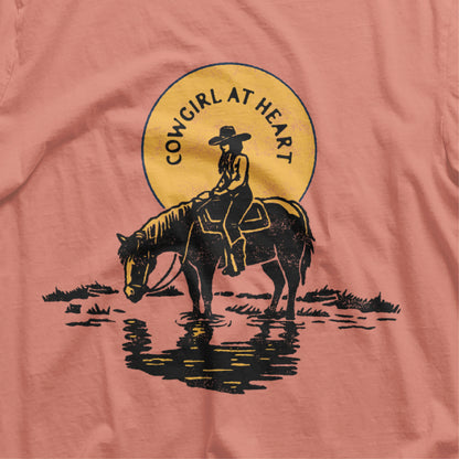 Cowgirl at Heart Shirt featuring a silhouette of a cowgirl sitting on a horse by a river, perfect for equestrian and horse lovers.