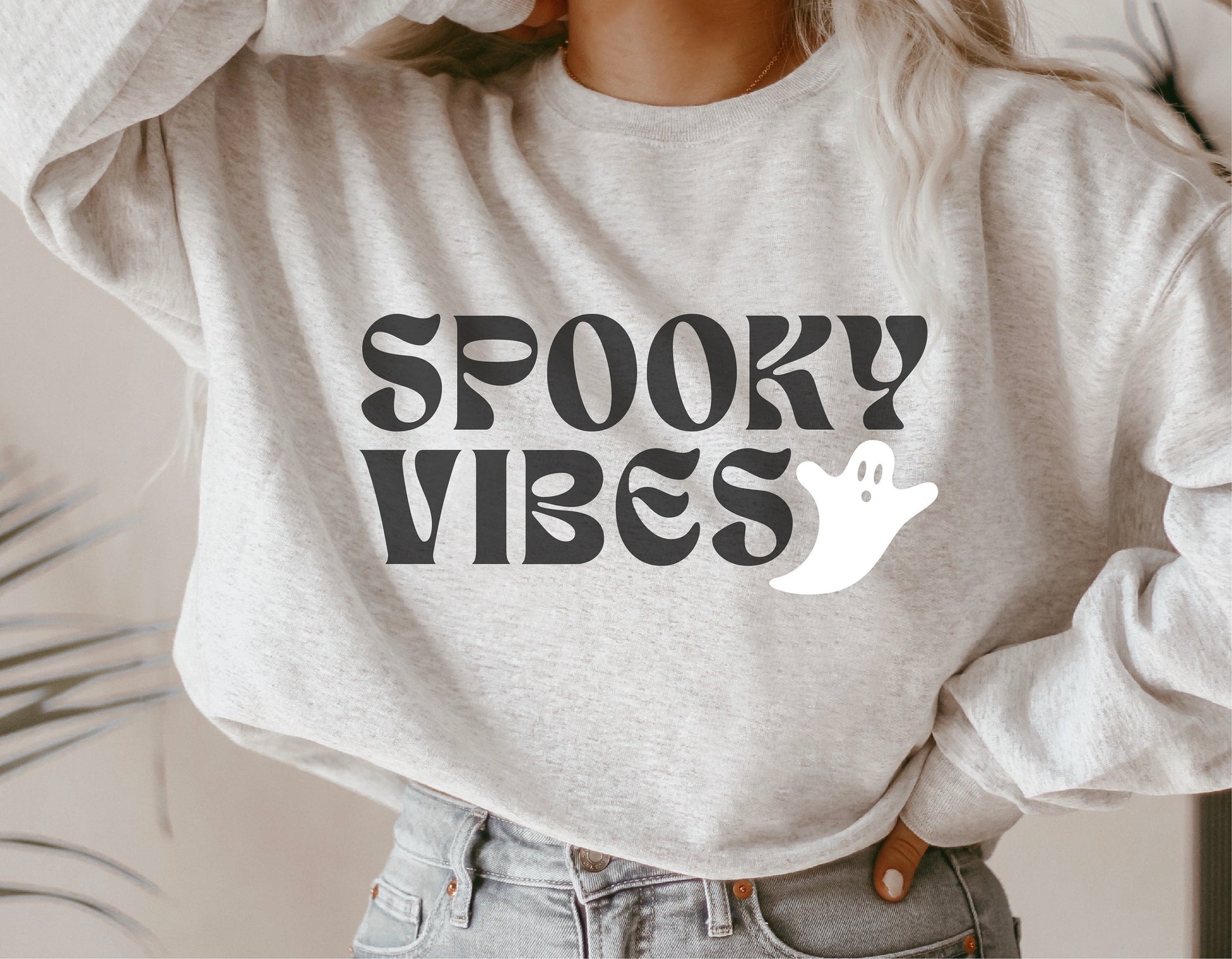 A woman wearing a grey sweatshirt featuring a "Spooky Vibes" design with a cute ghost graphic, perfect for Halloween and autumn decor.