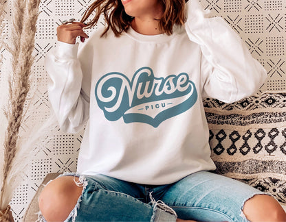 PICU Nurse logo on white sweatshirt, worn by person sitting on couch decorated with modern patterns; cozy, retro, and trendy design.