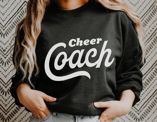 Black sweatshirt with white 'Cheer Coach' text, worn by individual, ideal for cheerleading coaches and team spirit apparel.