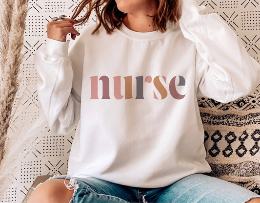 Person wearing a white sweatshirt with 'nurse' multi-colored letters, sitting casually on a patterned cushion.