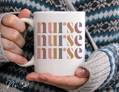 Person holding a white mug with multi-colored 'nurse' text design, wearing a gray knit sweater with black and white patterns.