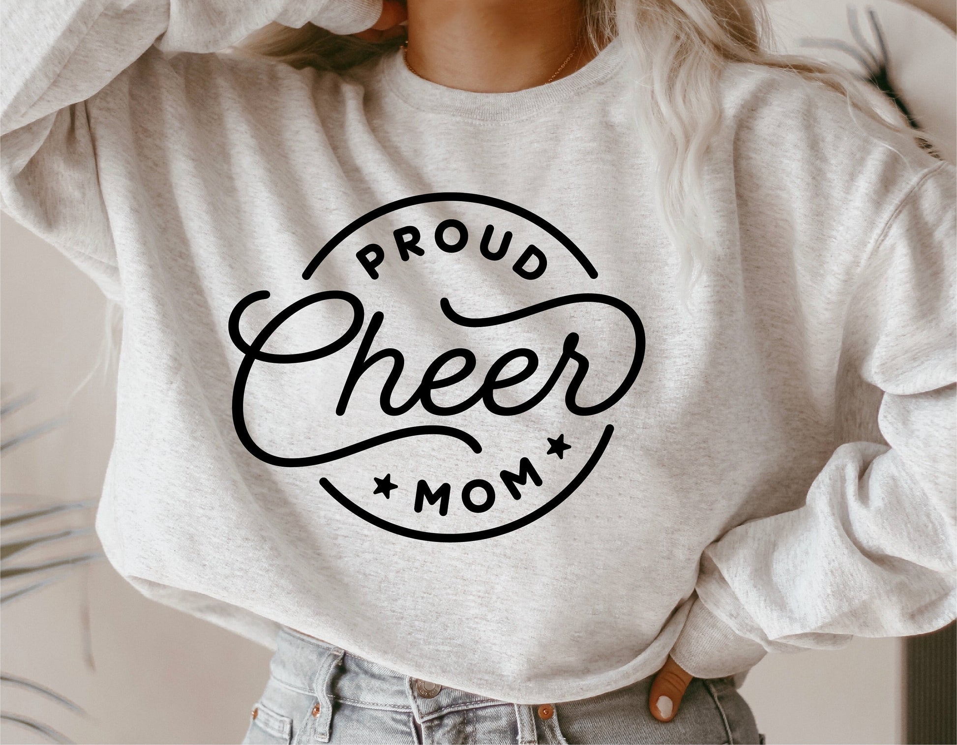 Woman wearing a sweater with 'Proud Cheer Mom' design, showcasing cheerleader support. Ideal for SVG, cut files, sublimation projects.
