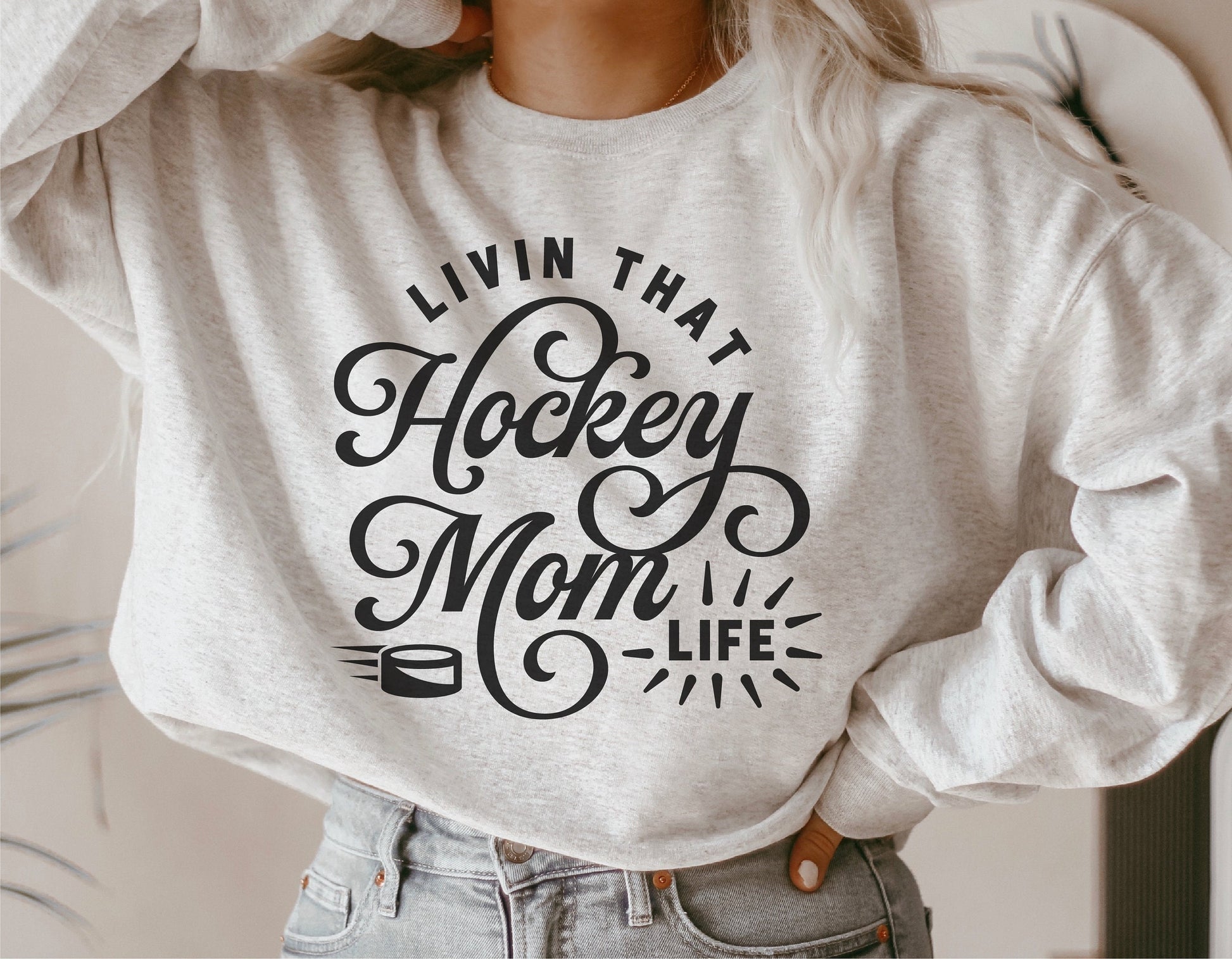 Woman wearing a sweatshirt with 'Livin That Hockey Mom Life' text design, ideal for Cricut and Silhouette projects.