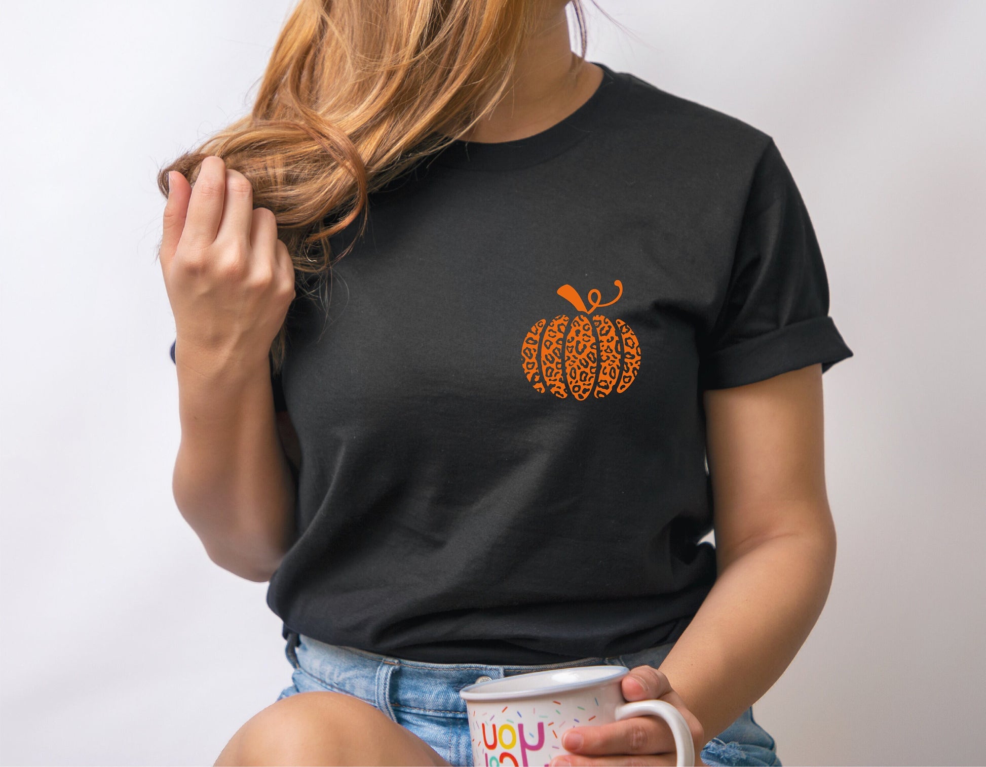 Woman wearing black t-shirt with leopard pumpkin design, holding a mug, showcasing fall fashion.