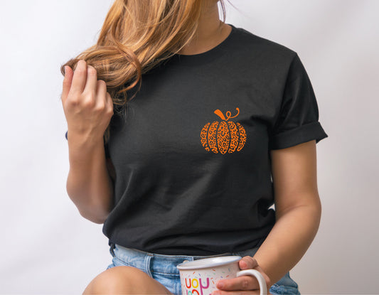 Woman wearing black t-shirt with leopard pumpkin design, holding a mug, showcasing fall fashion.